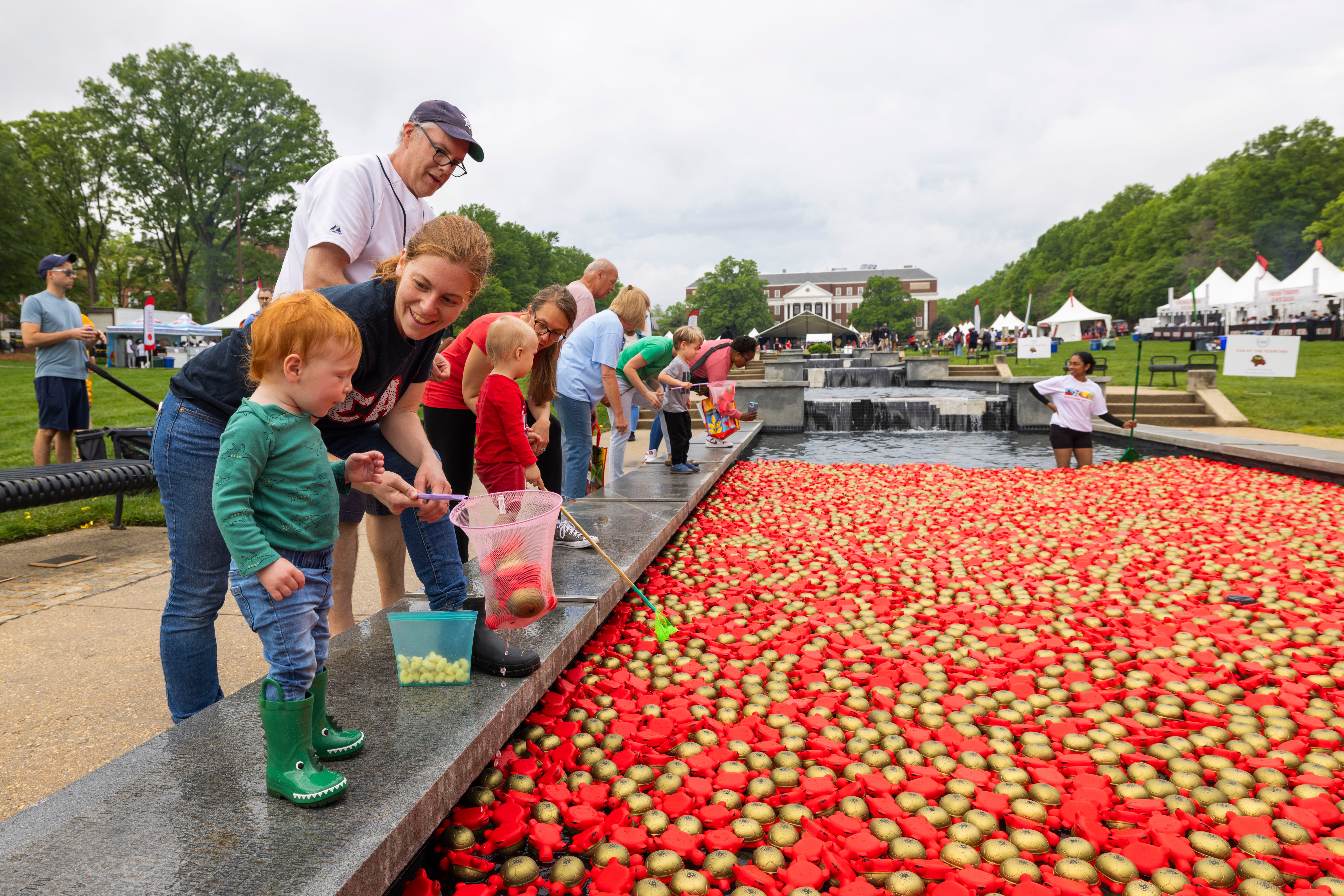 A mom squats down to eye level with her son. They are standing next to McKeldin fountain, full of foam turtles for Maryland Day. 