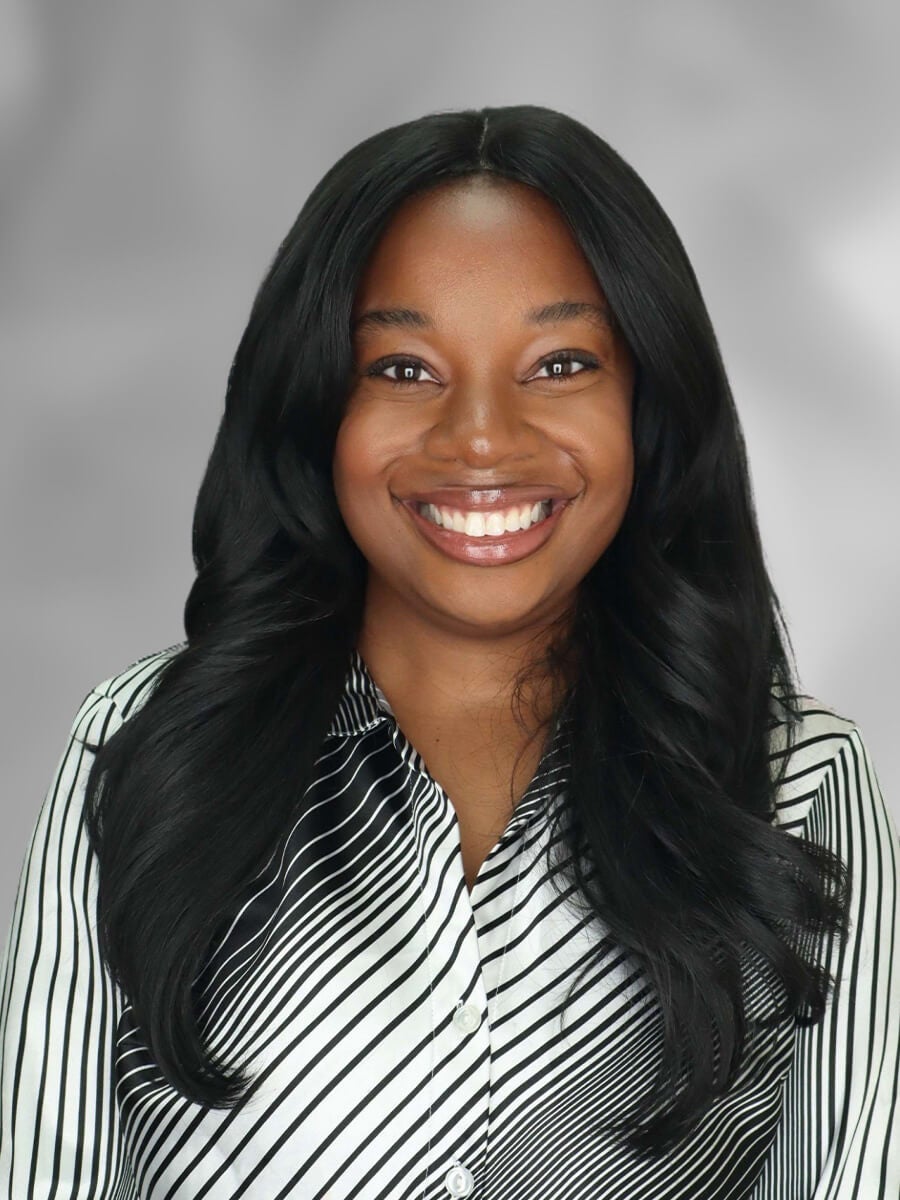 Zoe's headshot features a woman smiling with long black hair wearing a gray and white button down shirt.