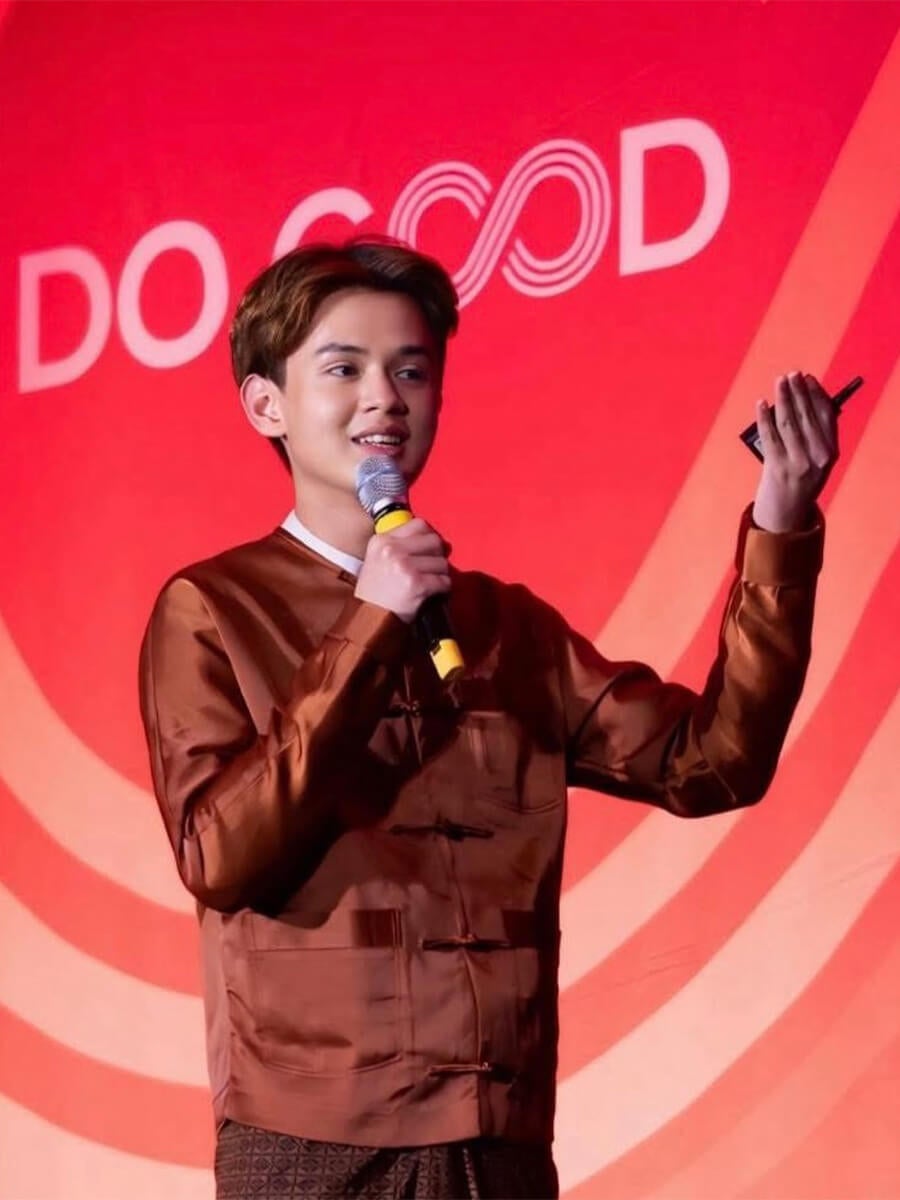 Headshot of a man speaking with a mic in his hand with a red banner in the background
