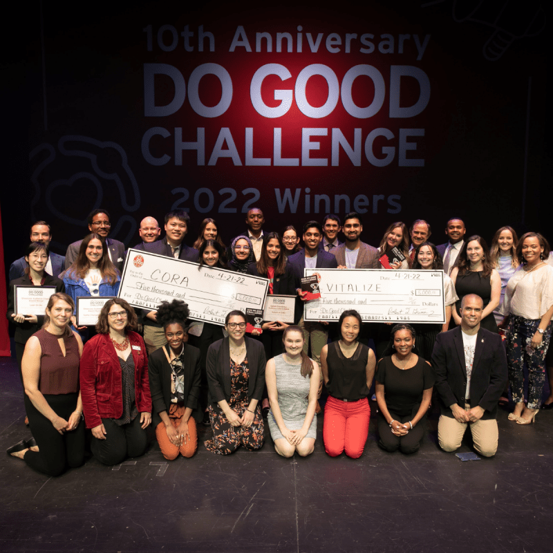 All particpants in Do Good Challenge pose on stage with checks