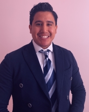 Carlos Orbe is wearing a suit and tie and smiling. 