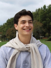Emilian Nakov's headshot. He's wearing a sweater with cardigan tied around his neck. The background features a blurry cloudy day with green trees.