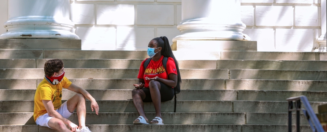 students with masks sitting on building steps