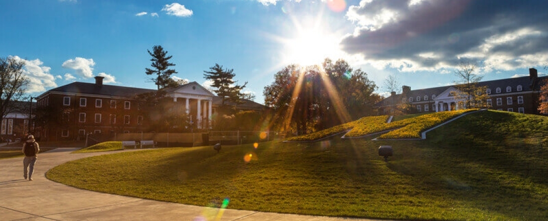 The sun is shining brightly over a landscape image with a building on UMD's campus. 