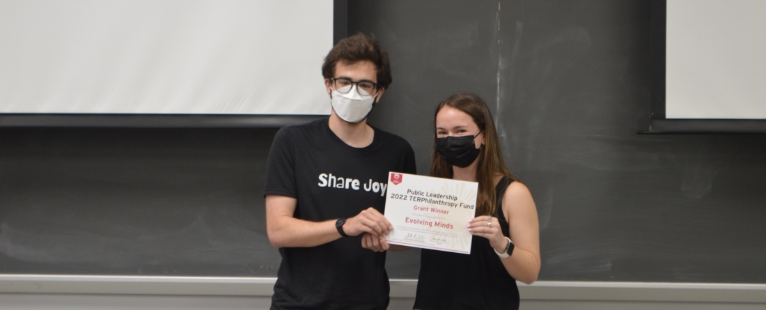 A man and a woman are standing and holding an award for a 1,000 dollar grant. 