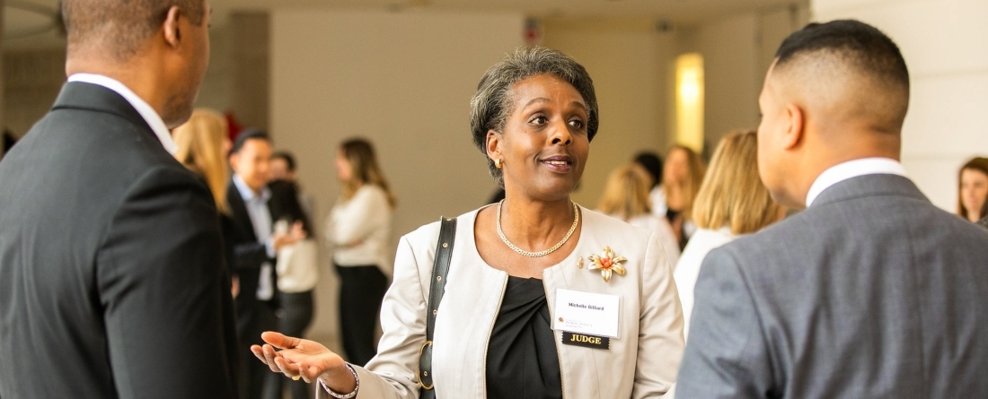A woman is standing and speaking with enthusiasm to two men.