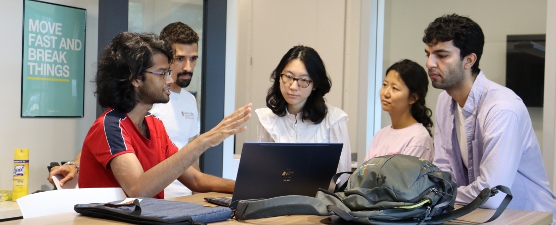 A group of students gathered around a laptop discussing with each other. 