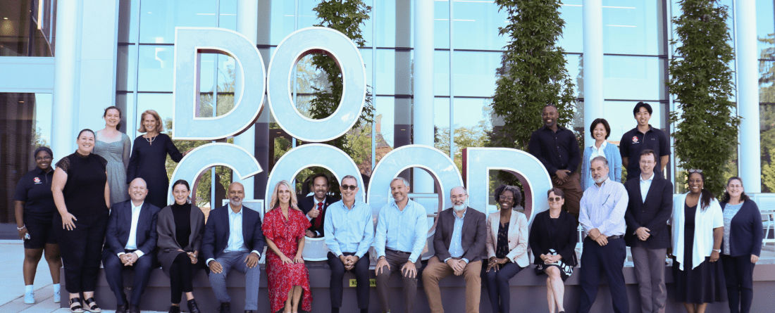 group of individuals standing beside and sitting in front of the Do Good scultupre