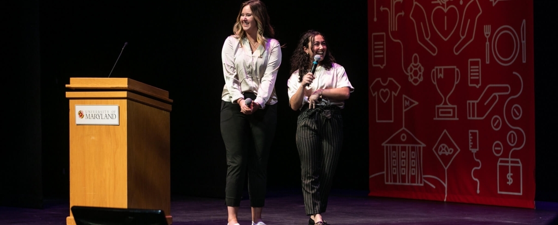 Two students on stage in white shirts speaking