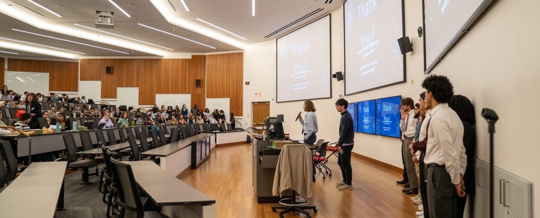 Students stand presenting in front of a lecture hall