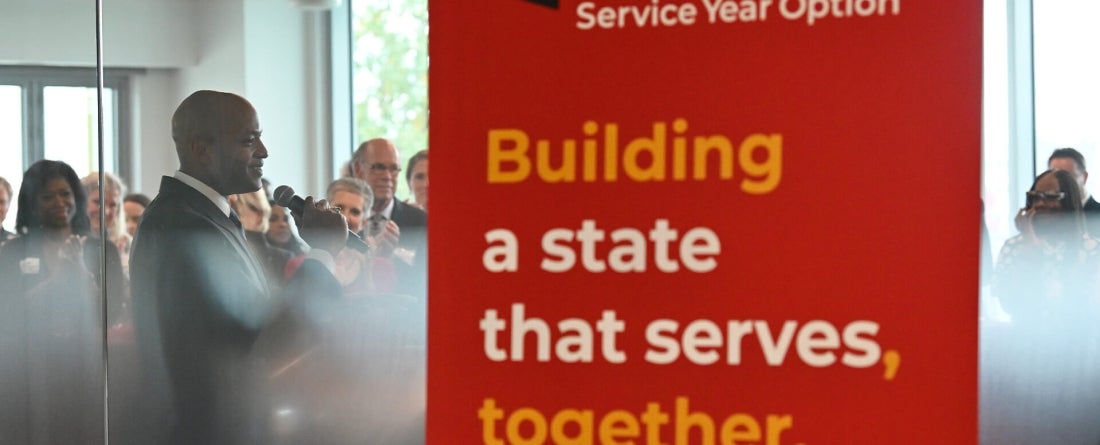 Image includes a red banner in front of a glossy window that says Building a state that serves together.